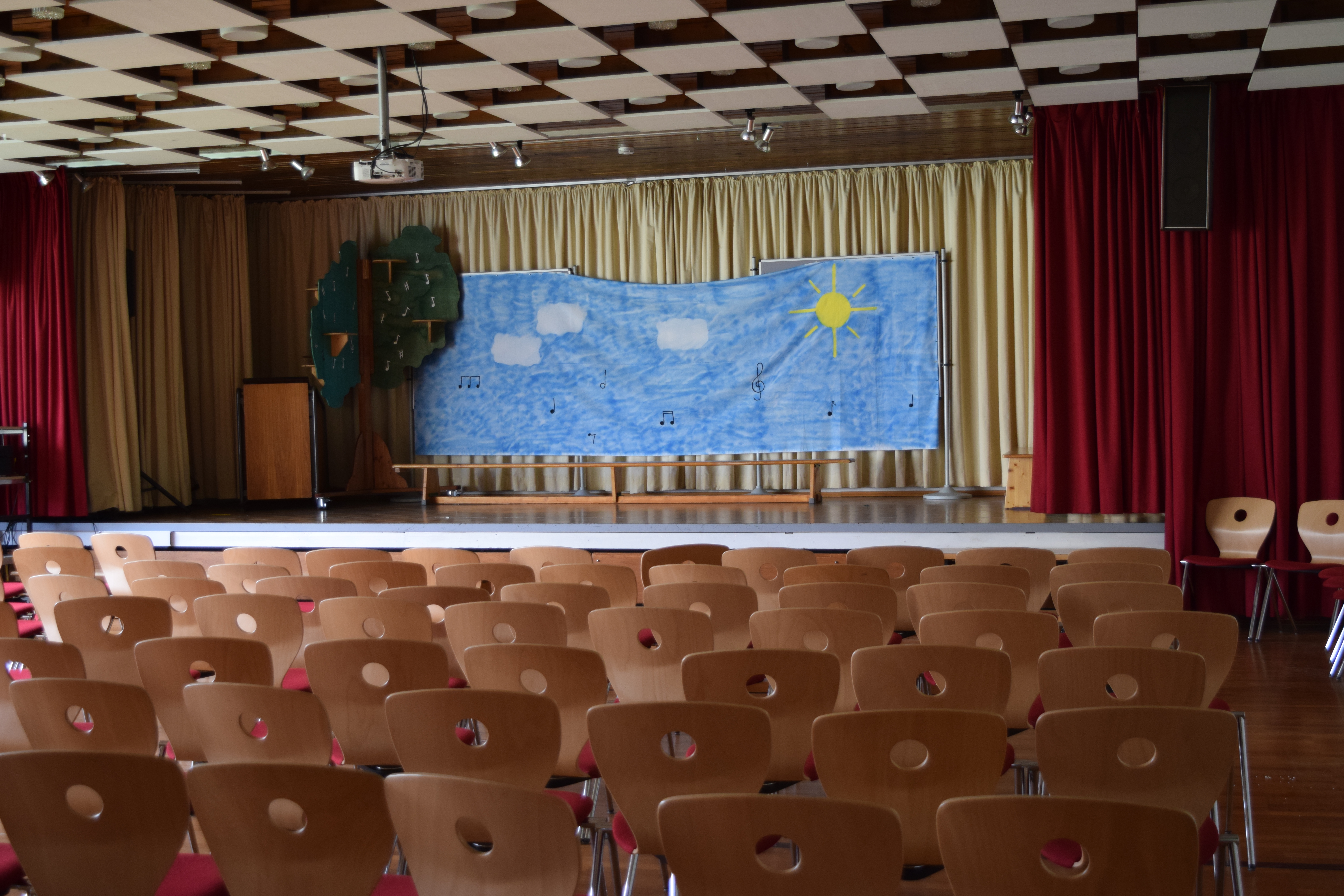 Eine Aula mit vielen Stühlen vor einer Bühne.